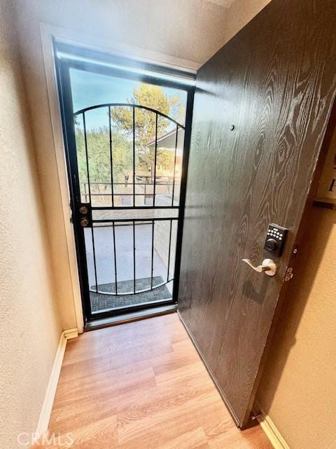 doorway to outside featuring baseboards, light wood-style floors, and a textured wall