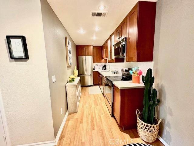 kitchen with visible vents, stainless steel appliances, light wood-style floors, light countertops, and baseboards