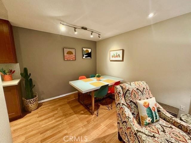 dining room featuring rail lighting, light wood-type flooring, and baseboards