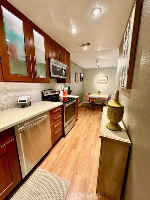 kitchen with light wood-type flooring, visible vents, appliances with stainless steel finishes, light countertops, and glass insert cabinets