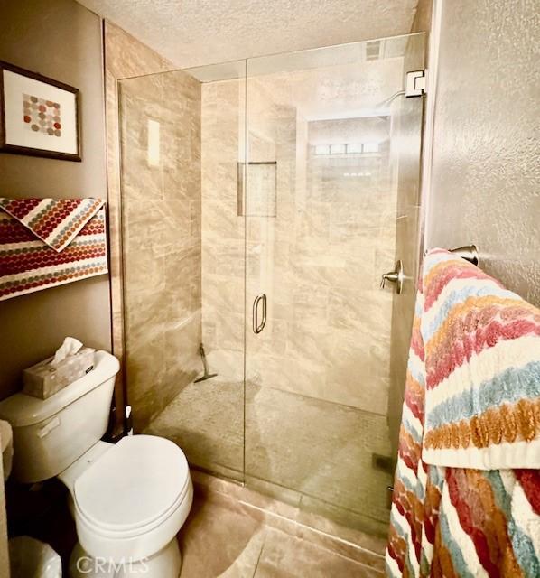 bathroom featuring a textured ceiling, a stall shower, and toilet