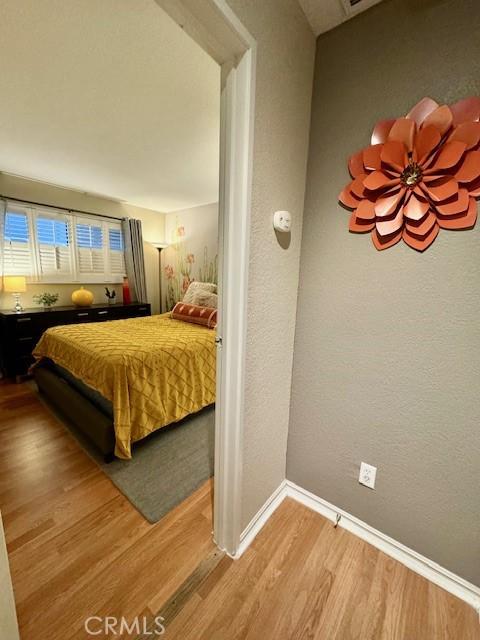 bedroom featuring baseboards, wood finished floors, and a textured wall