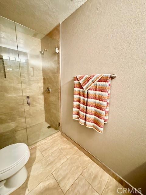 bathroom featuring tile patterned floors, a shower stall, toilet, and a textured wall