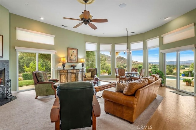 living room with a mountain view, ceiling fan with notable chandelier, a high end fireplace, and light hardwood / wood-style flooring