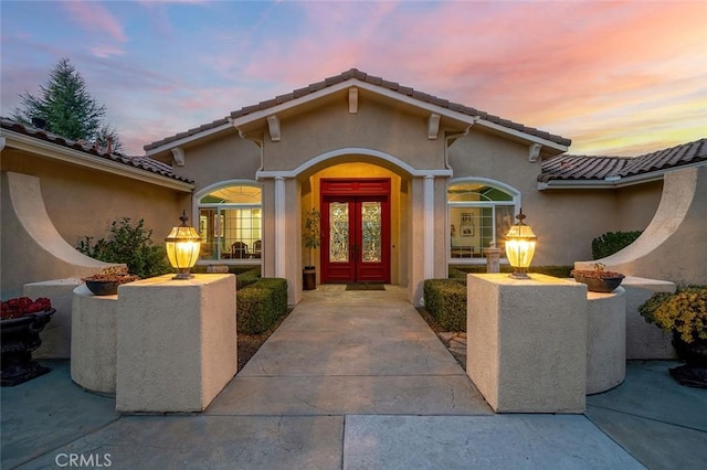 doorway to property featuring a tile roof, french doors, and stucco siding