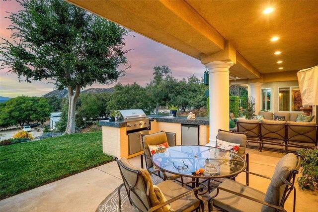 patio terrace at dusk with an outdoor kitchen, an outdoor hangout area, and a grill