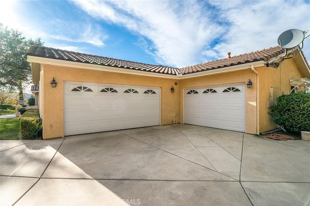 view of front facade with concrete driveway, a tiled roof, a garage, and stucco siding