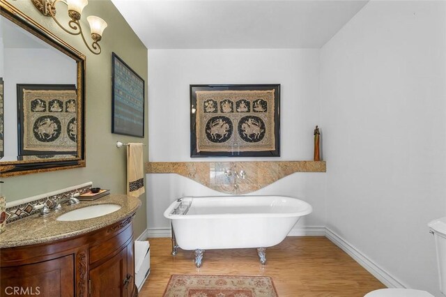 full bathroom with toilet, a freestanding bath, vanity, and wood finished floors