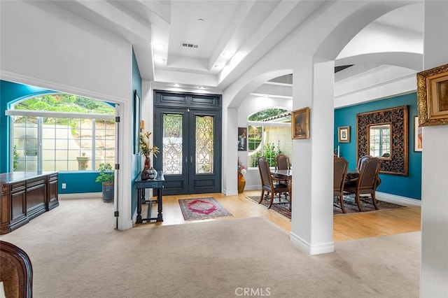 entryway featuring a raised ceiling, plenty of natural light, light colored carpet, and french doors