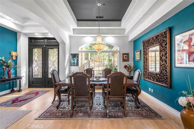 dining room with a tray ceiling, arched walkways, wood finished floors, and french doors