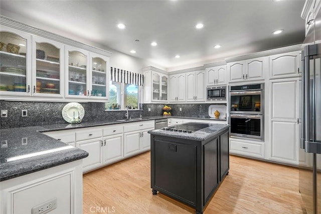 kitchen with dark stone countertops, a sink, white cabinets, light wood-style floors, and appliances with stainless steel finishes