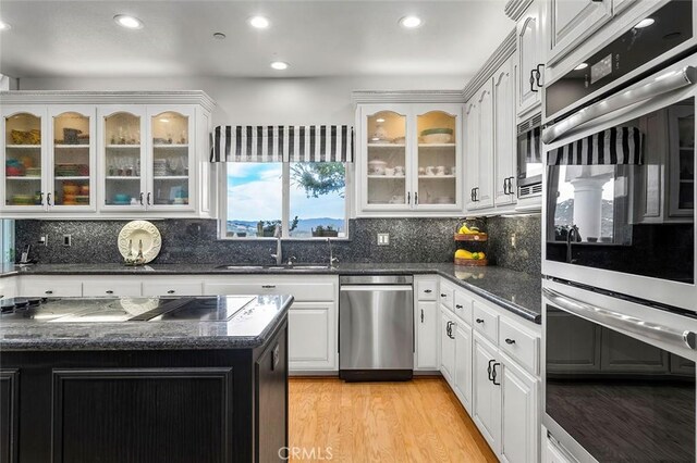 kitchen featuring stainless steel appliances, tasteful backsplash, dark stone counters, light hardwood / wood-style floors, and white cabinets