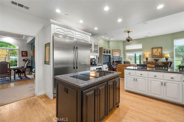 kitchen featuring light wood-type flooring, black electric cooktop, a kitchen island, ceiling fan, and white cabinetry