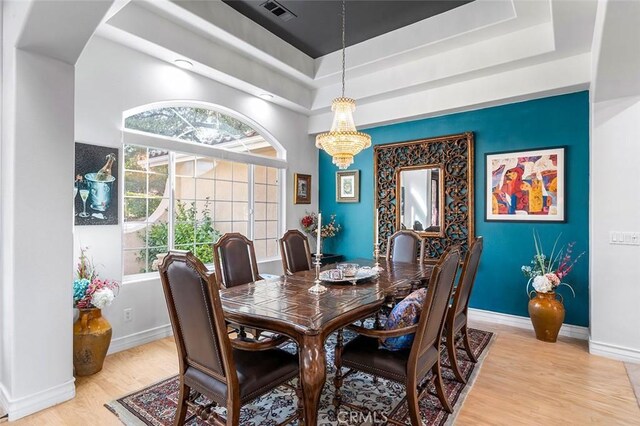 dining room with a notable chandelier, a raised ceiling, and light hardwood / wood-style flooring