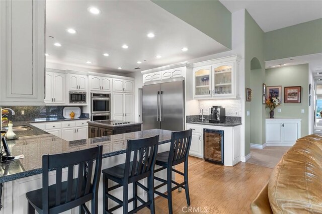 kitchen with white cabinets, a kitchen breakfast bar, built in appliances, kitchen peninsula, and beverage cooler