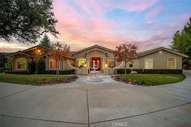 view of front of home with stucco siding, a lawn, driveway, and a tile roof