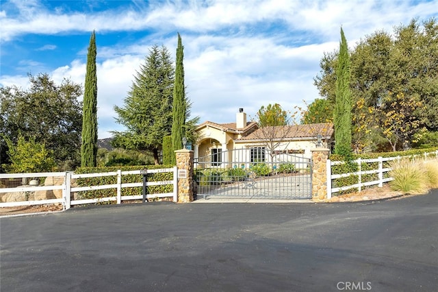 view of front facade with a fenced front yard, stucco siding, a chimney, and a gate