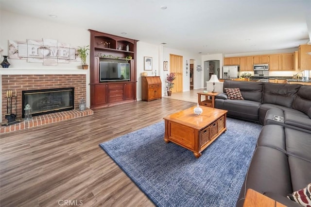 living room with a brick fireplace, dark wood-type flooring, and sink