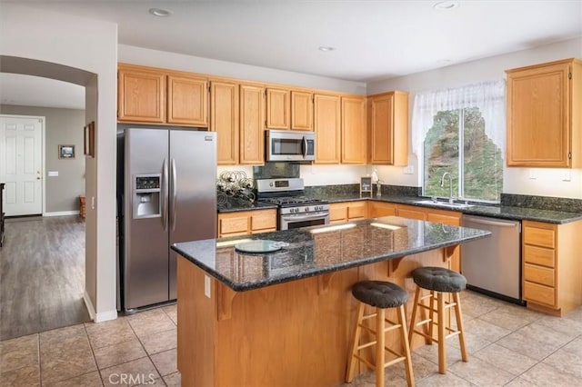 kitchen featuring sink, light tile patterned floors, dark stone countertops, a kitchen island, and stainless steel appliances