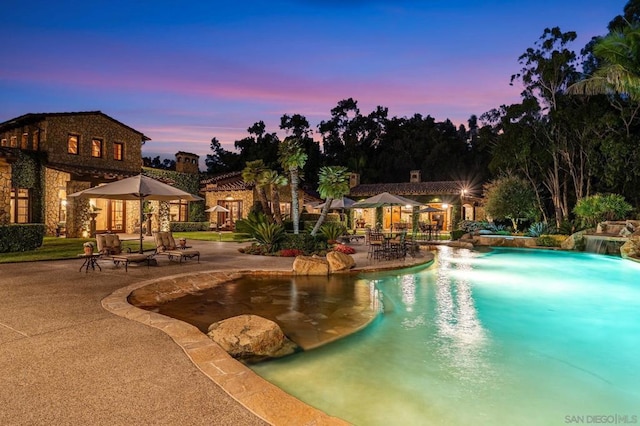 pool at dusk featuring a patio and pool water feature