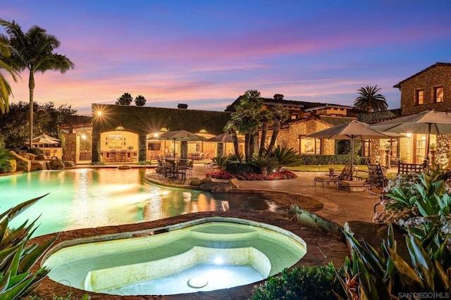 pool at dusk with a patio area and an in ground hot tub