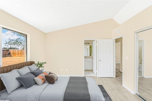 bedroom with a textured ceiling, ensuite bathroom, light hardwood / wood-style flooring, and lofted ceiling