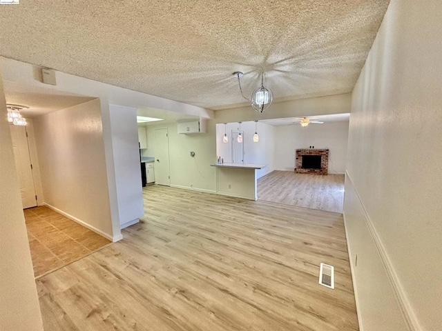 unfurnished living room with a textured ceiling, a notable chandelier, light hardwood / wood-style floors, and a fireplace