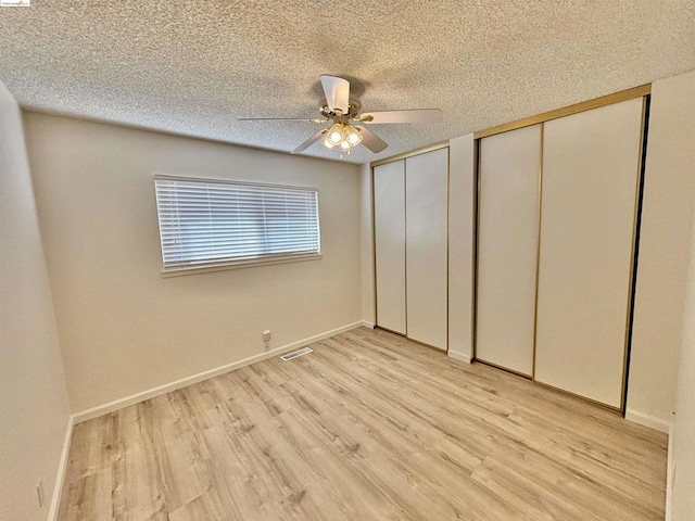 unfurnished bedroom with ceiling fan, light wood-type flooring, a textured ceiling, and multiple closets