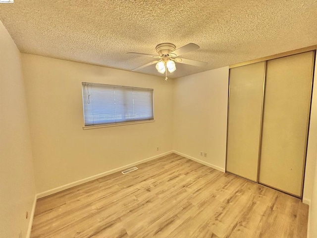 unfurnished bedroom featuring ceiling fan, a closet, a textured ceiling, and light wood-type flooring