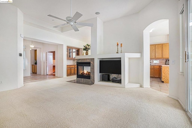 living room featuring ceiling fan, a multi sided fireplace, light carpet, and high vaulted ceiling