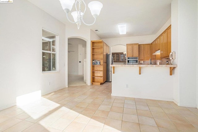 kitchen featuring kitchen peninsula, appliances with stainless steel finishes, a breakfast bar, a notable chandelier, and light tile patterned flooring