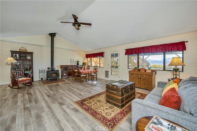 living room featuring a wood stove, ceiling fan, light hardwood / wood-style floors, and vaulted ceiling