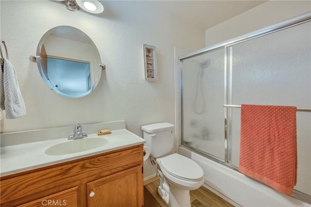 full bathroom featuring combined bath / shower with glass door, hardwood / wood-style floors, vanity, and toilet