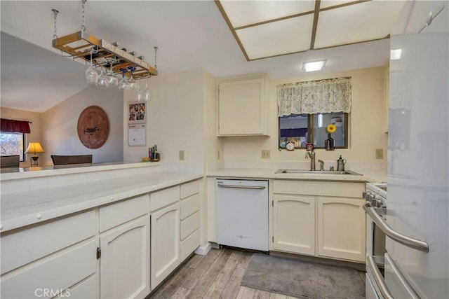 kitchen with kitchen peninsula, white appliances, sink, and light hardwood / wood-style flooring