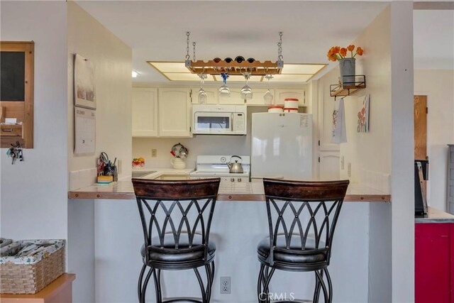 kitchen with white cabinetry, a breakfast bar, and white appliances