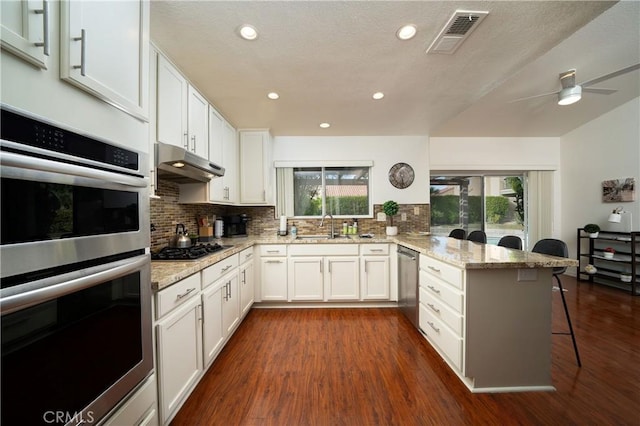 kitchen with appliances with stainless steel finishes, a breakfast bar, white cabinetry, light stone counters, and kitchen peninsula