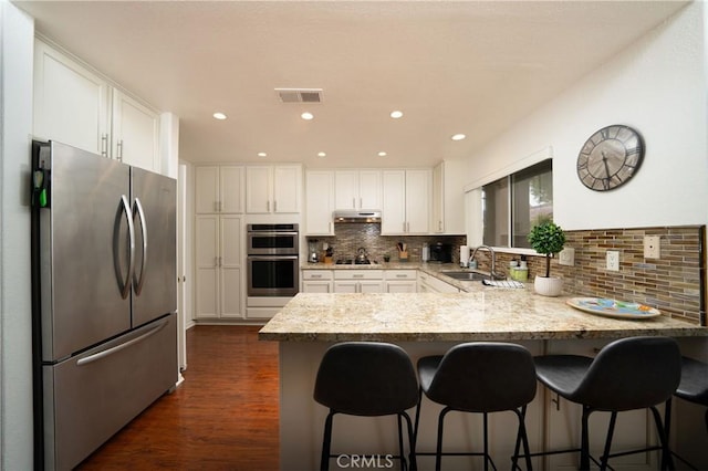 kitchen with sink, white cabinetry, light stone counters, appliances with stainless steel finishes, and decorative backsplash