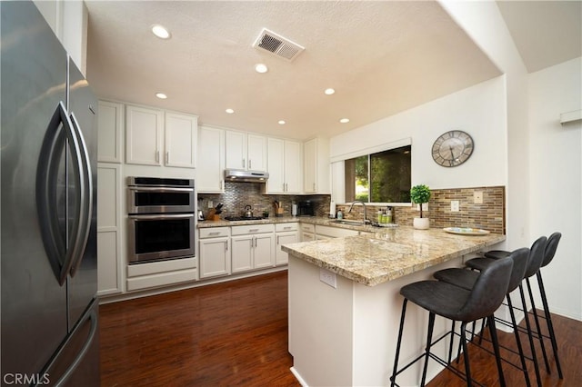 kitchen featuring appliances with stainless steel finishes, white cabinetry, a kitchen bar, kitchen peninsula, and light stone countertops