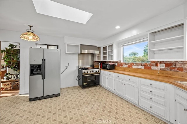 kitchen featuring black appliances, white cabinets, wall chimney range hood, hanging light fixtures, and a skylight