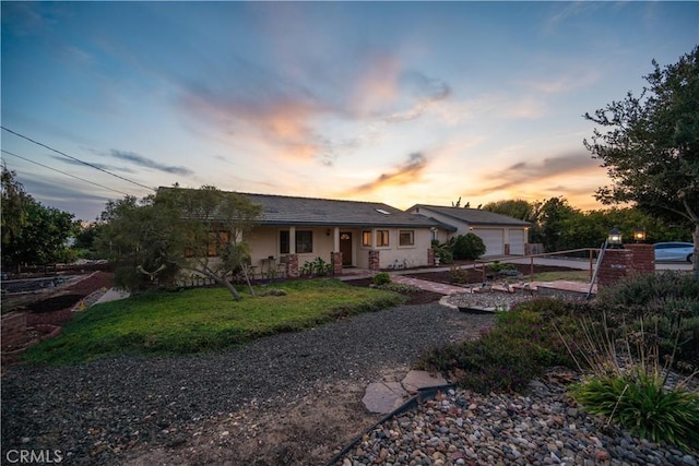 back of property at dusk featuring a garage, a lawn, and stucco siding