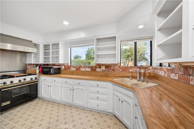 kitchen with wall chimney range hood, sink, black appliances, white cabinetry, and butcher block counters