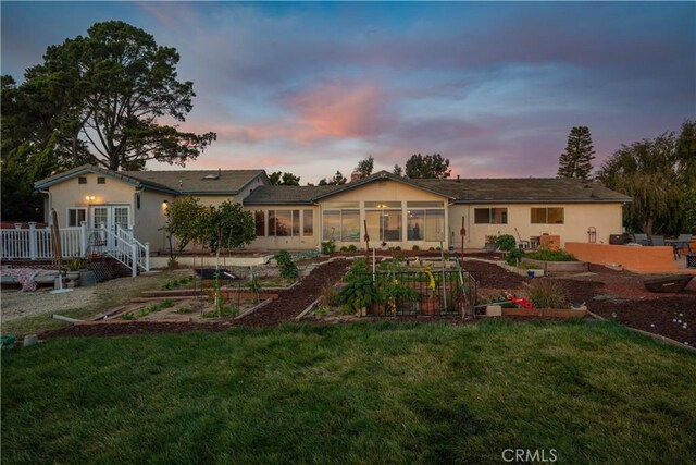 back house at dusk featuring a lawn and a sunroom