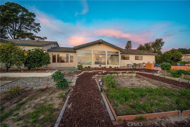 back house at dusk featuring a patio and a sunroom