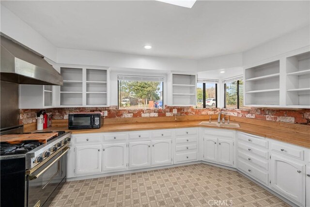 kitchen with backsplash, stainless steel stove, white cabinetry, and sink