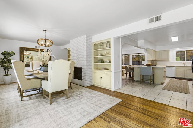 dining space featuring a brick fireplace, built in features, a notable chandelier, and light hardwood / wood-style flooring