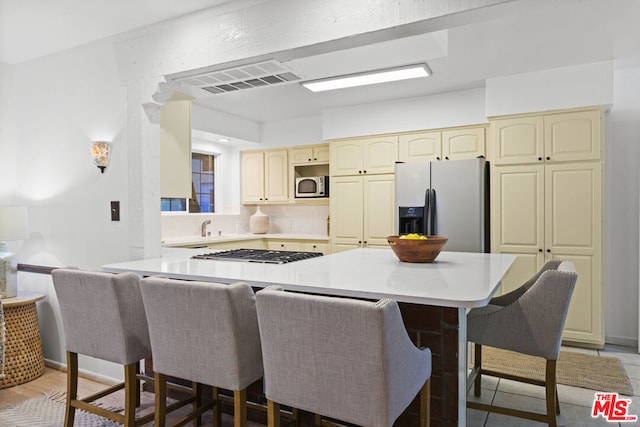 kitchen featuring a breakfast bar, kitchen peninsula, appliances with stainless steel finishes, and cream cabinetry