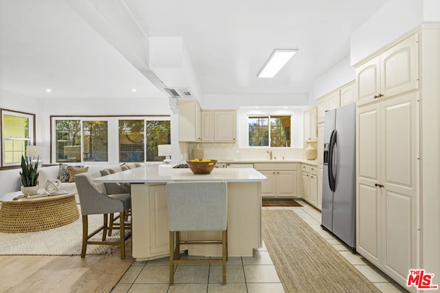 kitchen featuring stainless steel fridge with ice dispenser, light tile patterned floors, a breakfast bar area, a center island, and sink