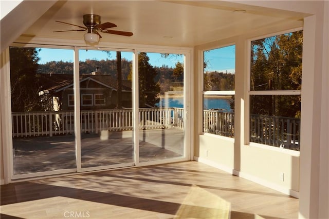 unfurnished sunroom featuring ceiling fan and a water view