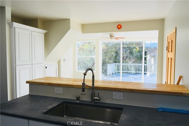 kitchen with ceiling fan, wooden counters, sink, and white cabinetry