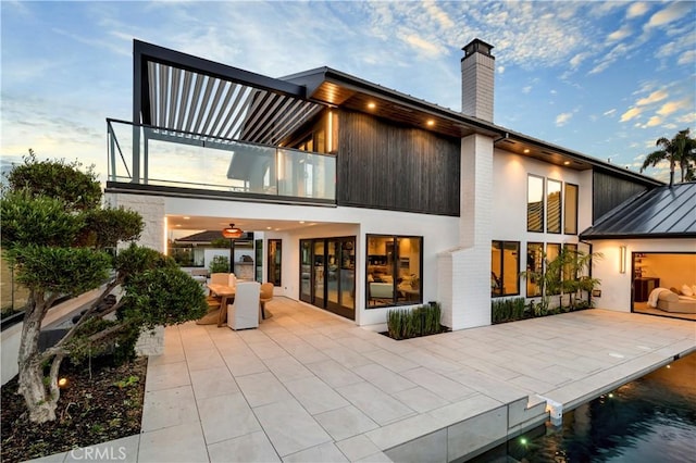 back house at dusk with a balcony and a patio